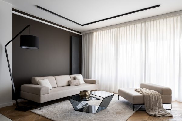 Simplicity and elegance in bright living room Simplicity and elegance in bright living room with big windows behind white curtains, big beige couch and seat, modern coffee table and black lamp